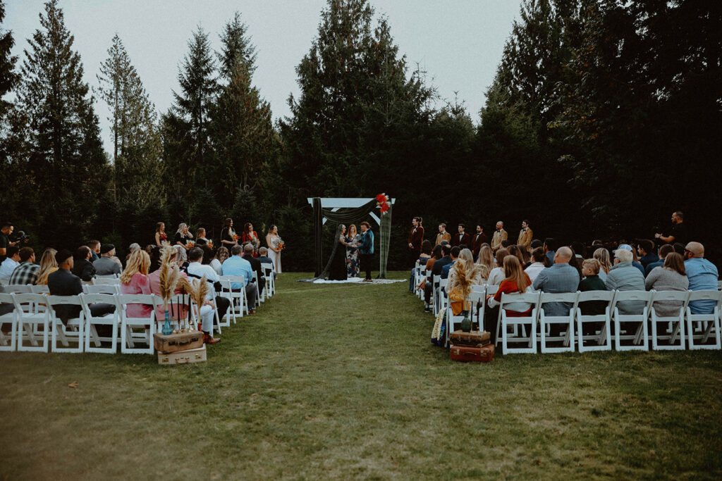 Washington couple sharing their wedding vows outside in their ceremony surrounded by evergreen trees, friends, and family