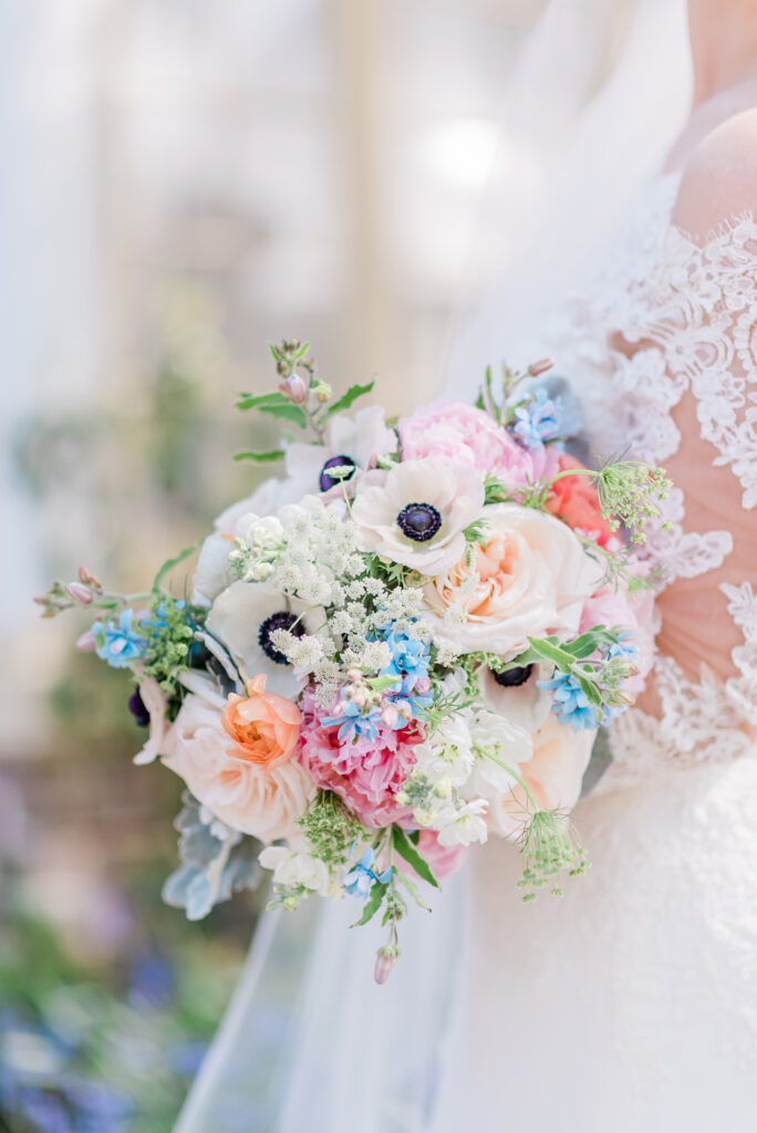 Delicate bridal bouquet with white anemones, peach garden roses, dusty miller, and colorful stock.