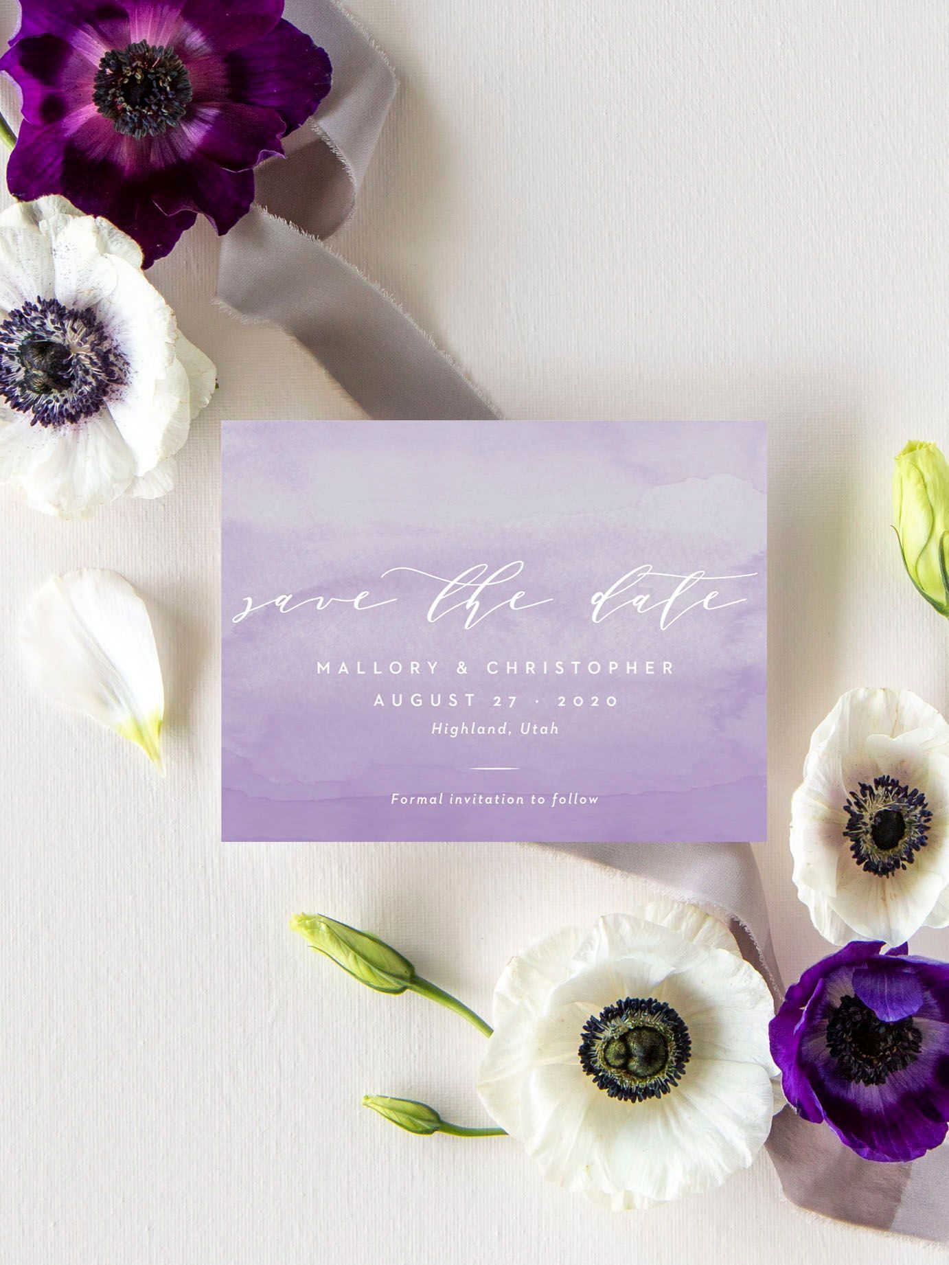 watercolored lilac wedding save the date with white script lettering surrounded by white and purple anemone flowers