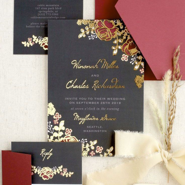 black wedding invitation with gold foiled cursive lettering, red and white florals and a red envelope