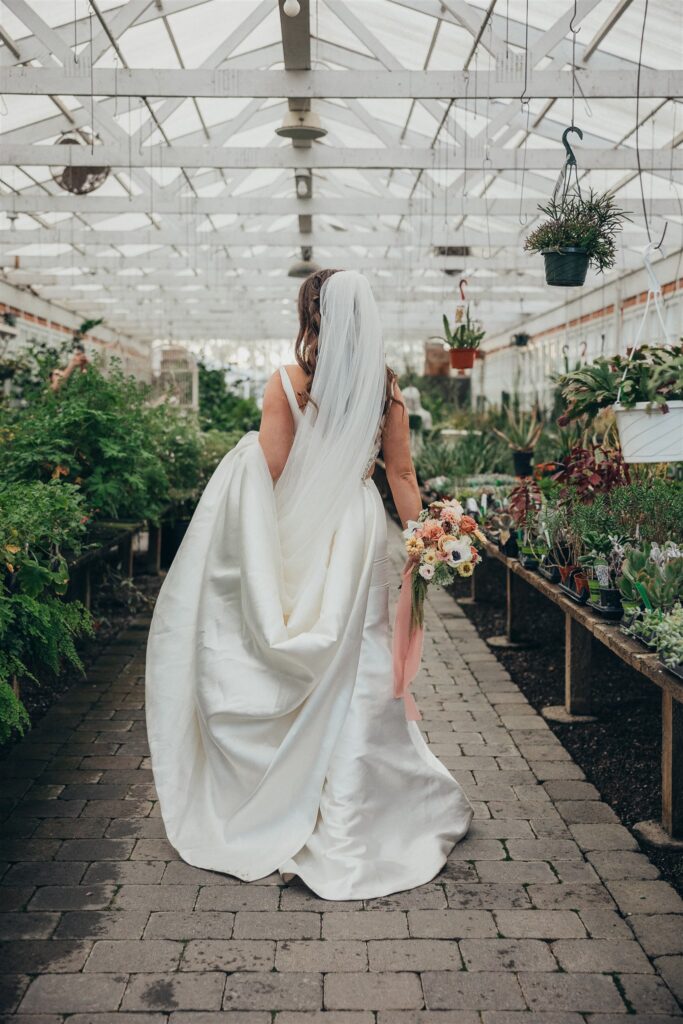 Bride walking through a greenhouse filled with plants at Christianson's Nursery, showcasing the beauty of garden wedding venues.
