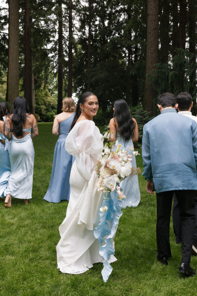 Bride walking with wedding party through lush gardens at Evergreen Gardens, a romantic Pacific Northwest garden wedding venue.