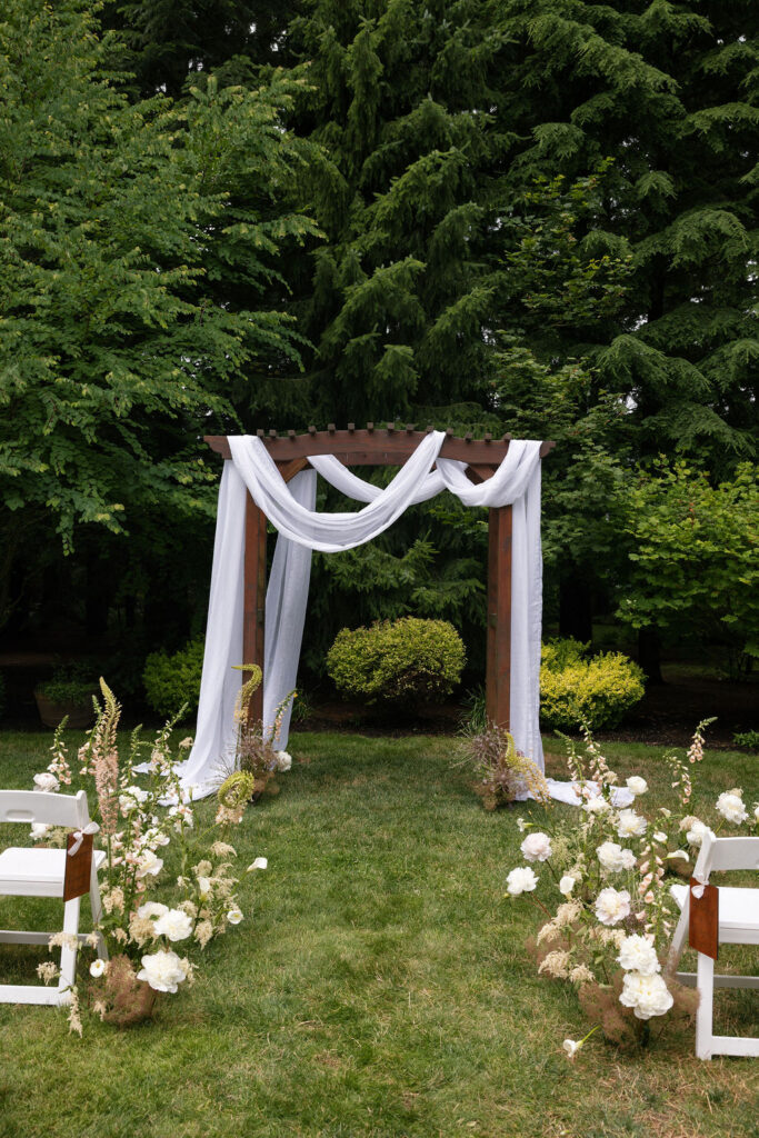 Ceremony arbor draped in white linen in the gardens at Evergreen Gardens, a beautiful Washington garden wedding venue.